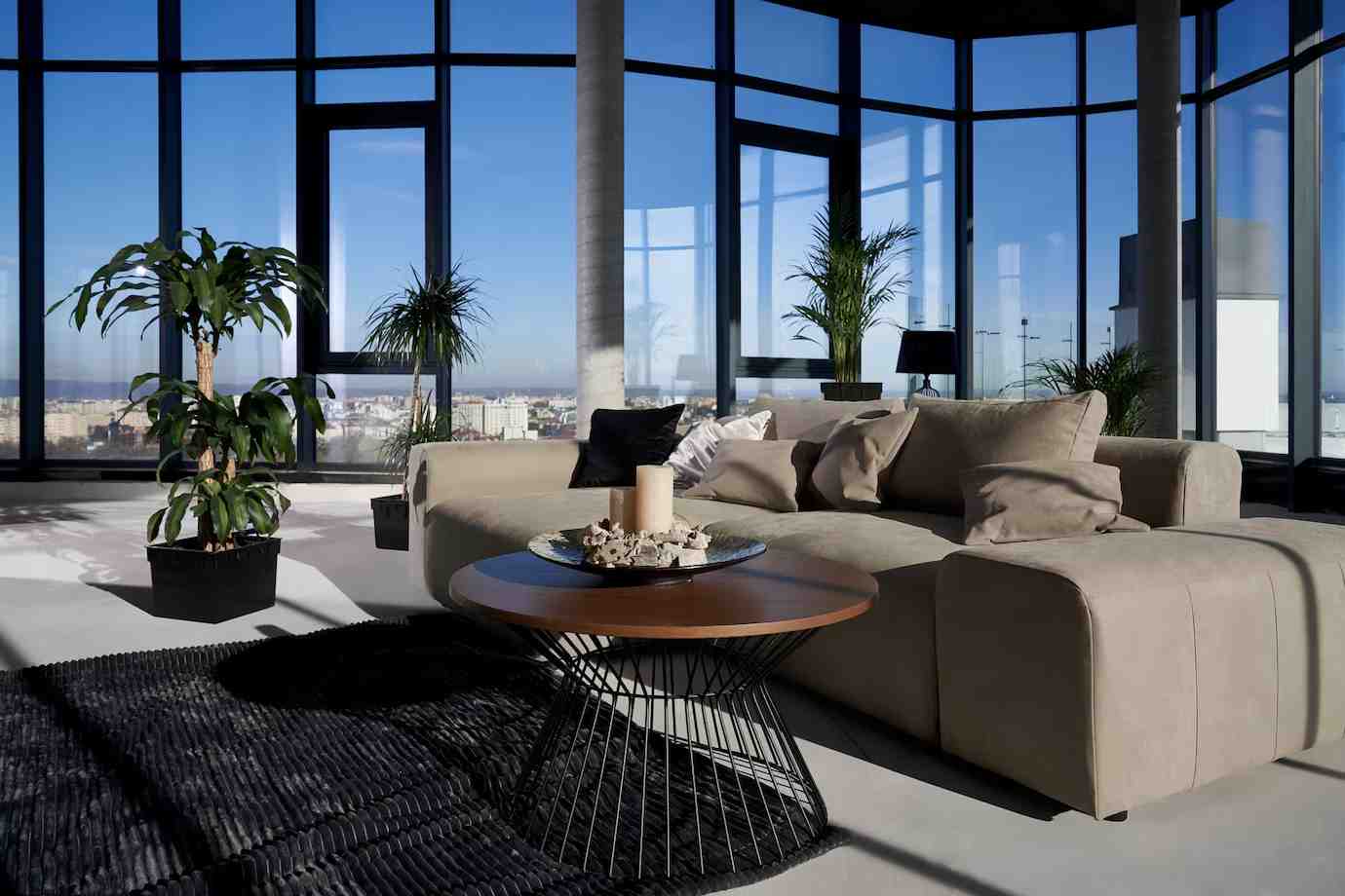 A modern living room with large windows, a cozy beige sectional sofa, a stylish round table
