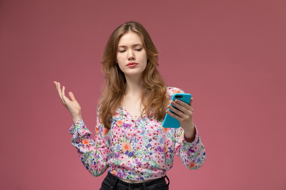 A woman in a floral shirt gestures with one hand while holding a blue smartphone in the other