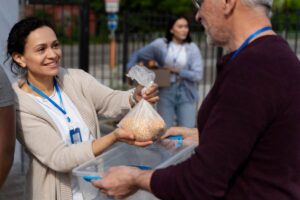 A woman volunteer hands a bag of beans to an elderly man at a food distribution event.