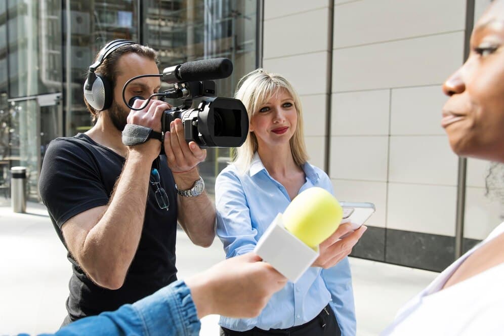 A cameraman filming a female reporter interviewing a woman on a city street.