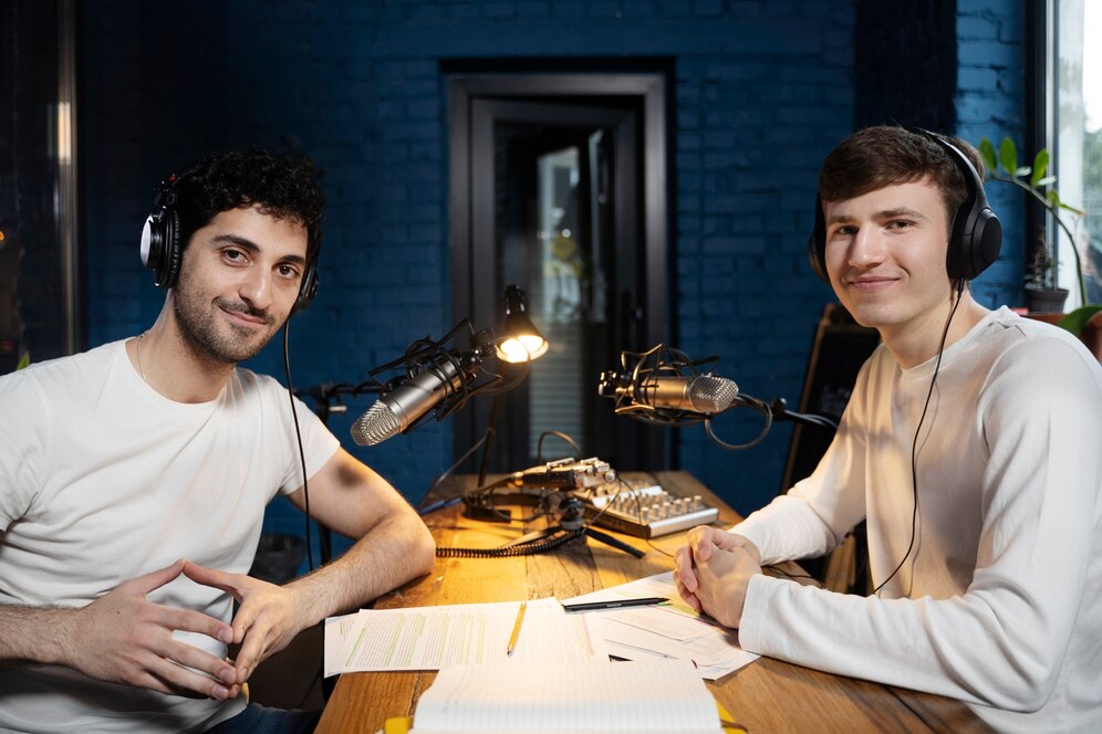Two men smiling and recording a podcast in a studio with microphones and audio equipment.
