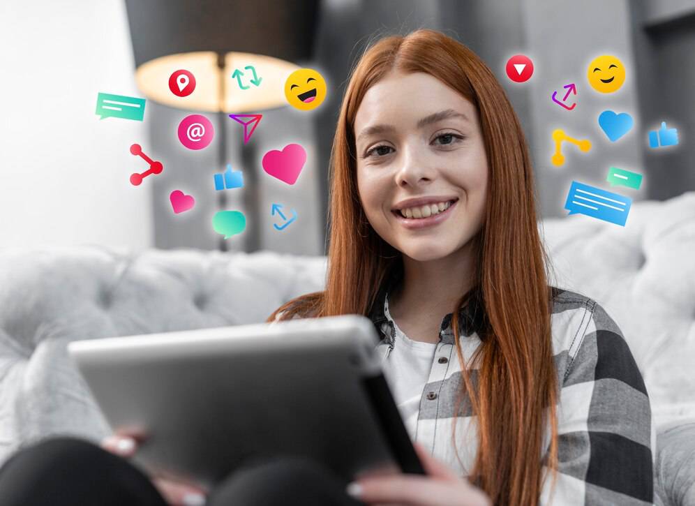 A person with long red hair sits on a couch, using a tablet surrounded by colorful social media icons