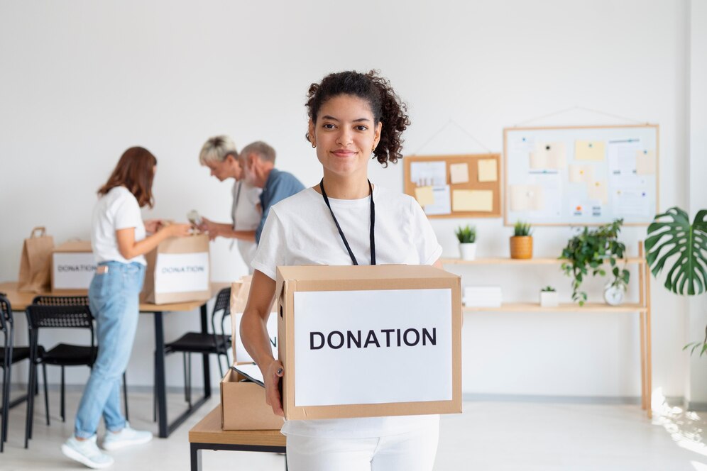 Young woman holding a donation box in a busy volunteer workspace.