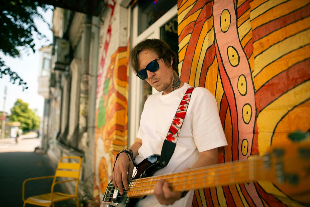 Man playing an electric guitar near a vibrant, colorful mural on a sunny street.