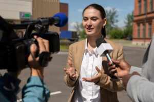 Woman being interviewed by news reporters outdoors, speaking into a microphone.