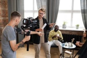 A film crew recording a scene in a loft, with a director giving instructions to actors and cameraman.