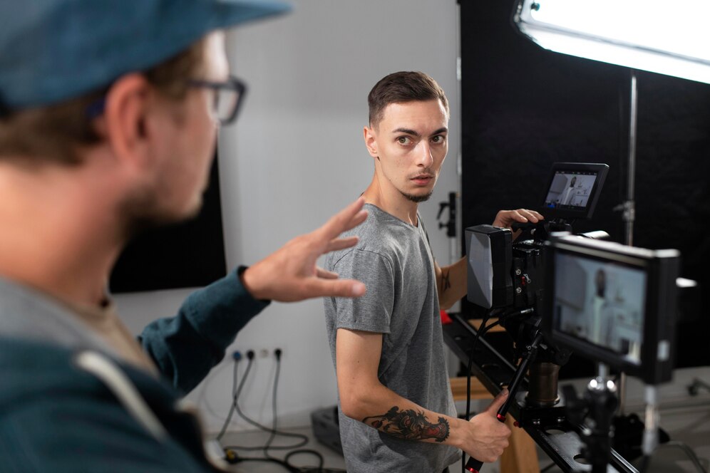 Two men in a video production studio, one operating the camera and the other directing.