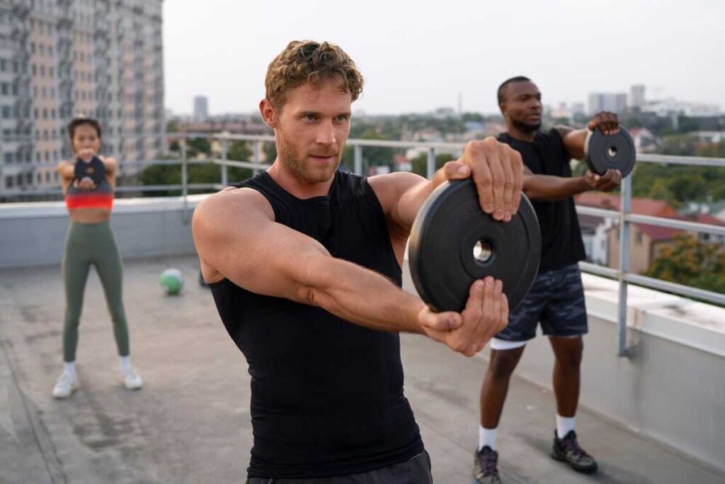 Three people exercising with weights on a rooftop, cityscape in the background.