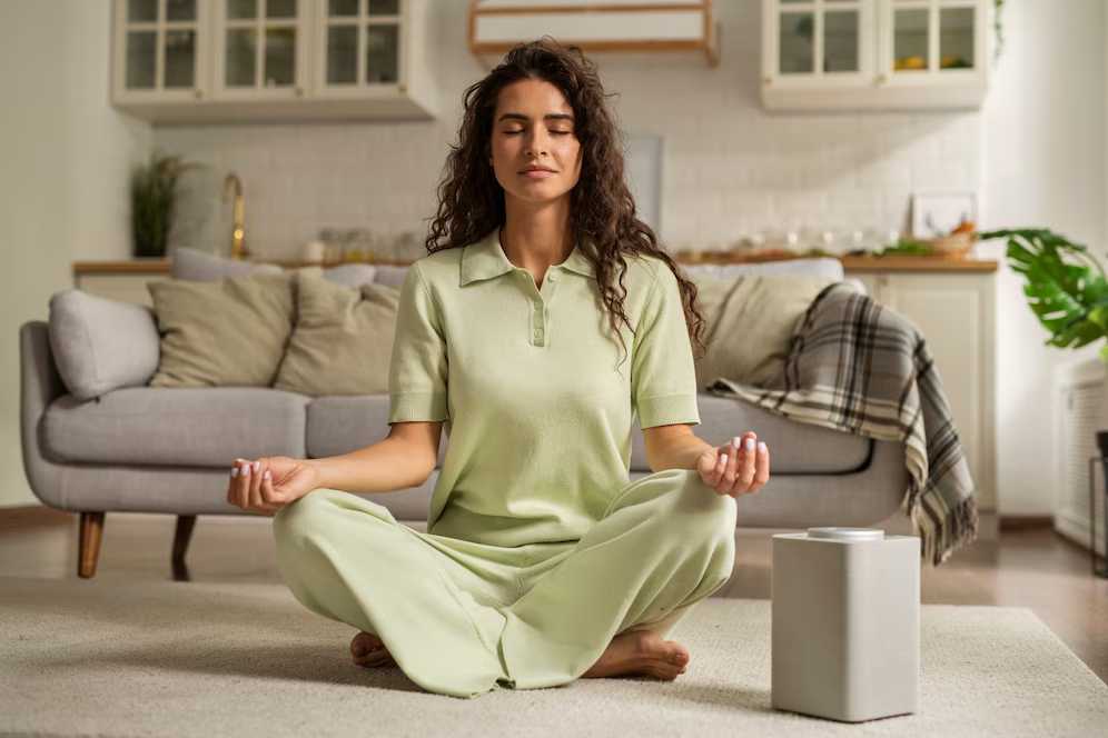 Woman meditating on a carpet in a cozy living room, dressed in a light green outfit.