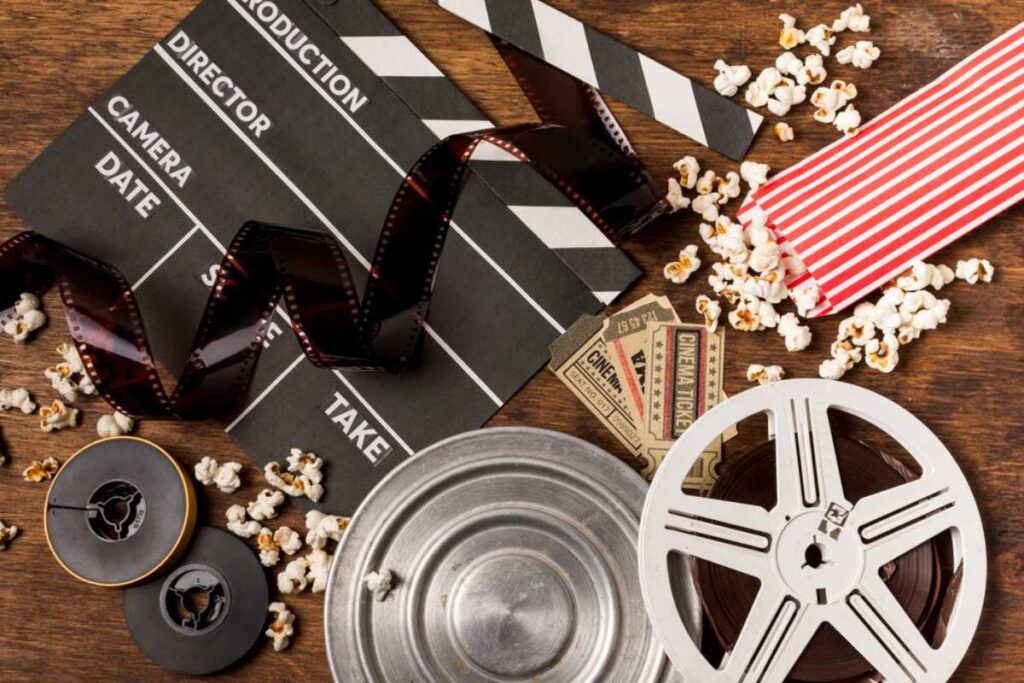 A movie clapperboard, film reels, and scattered popcorn on a wooden surface.