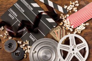 A movie clapperboard, film reels, and scattered popcorn on a wooden surface.