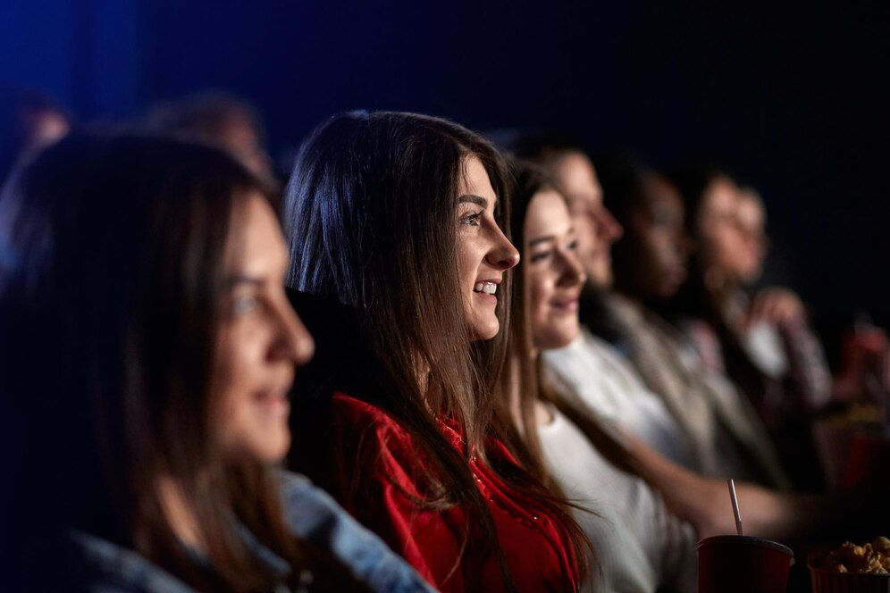 Group of people enjoying a movie in a cinema, smiling and holding snacks.