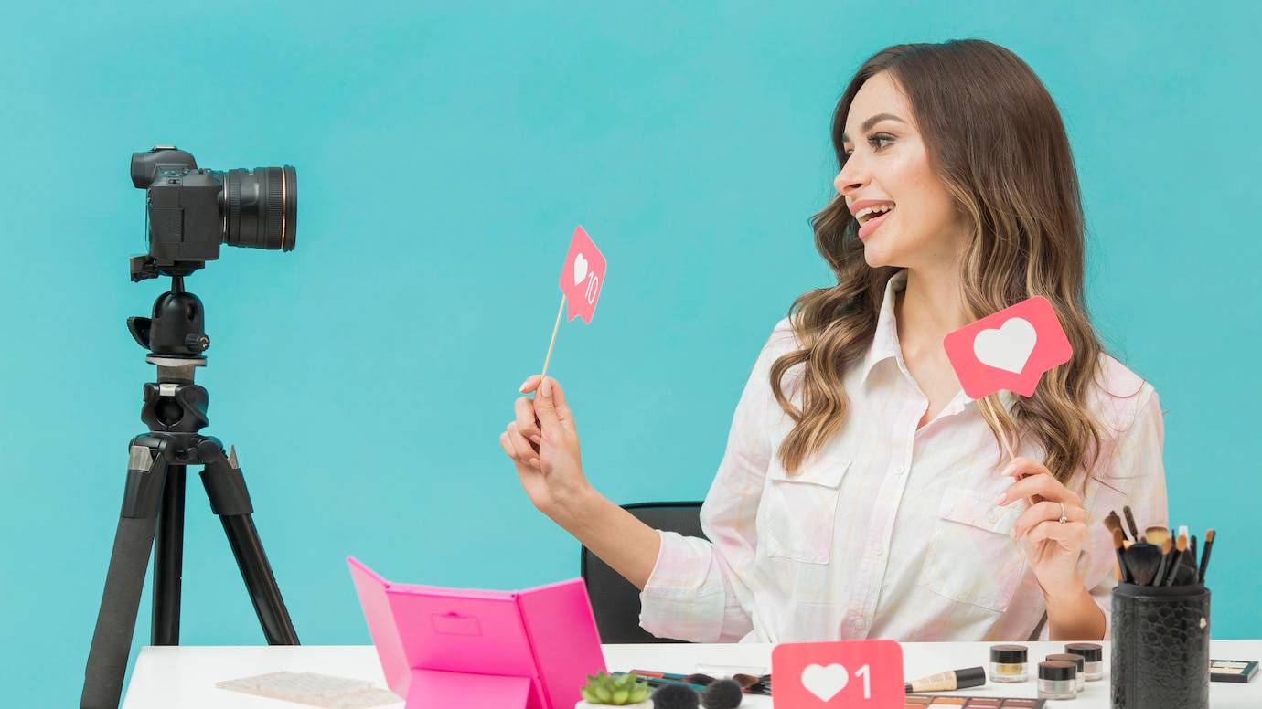 A content creator holds signs with love icons while seated at a makeup table